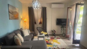 A living room with a sofa, a chair, a TV, and a colorful rug. - Holiday apartment with air conditioning and balcony (Poreč)