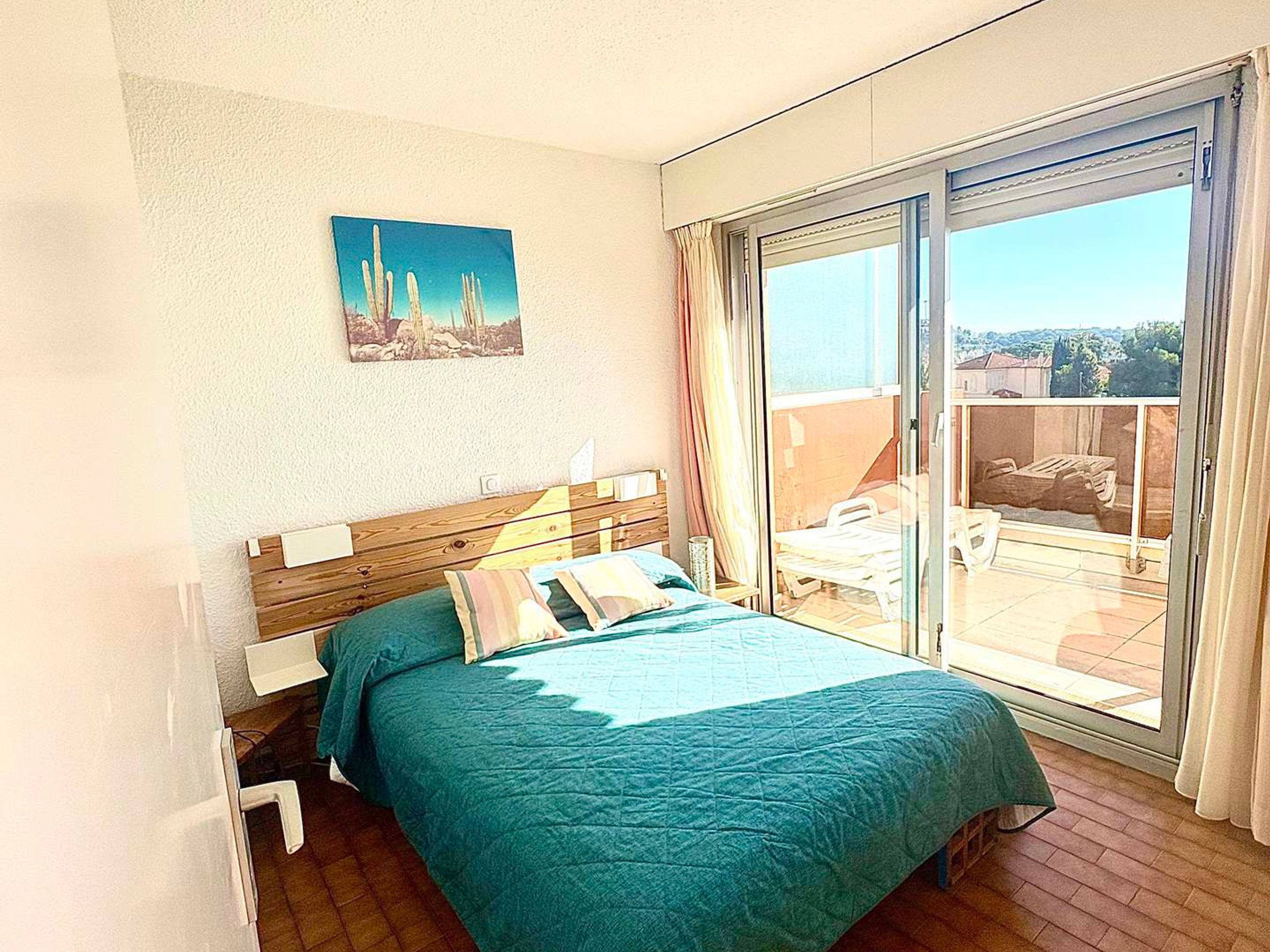 A bedroom with a bed, a painting, and a sliding glass door to a balcony.