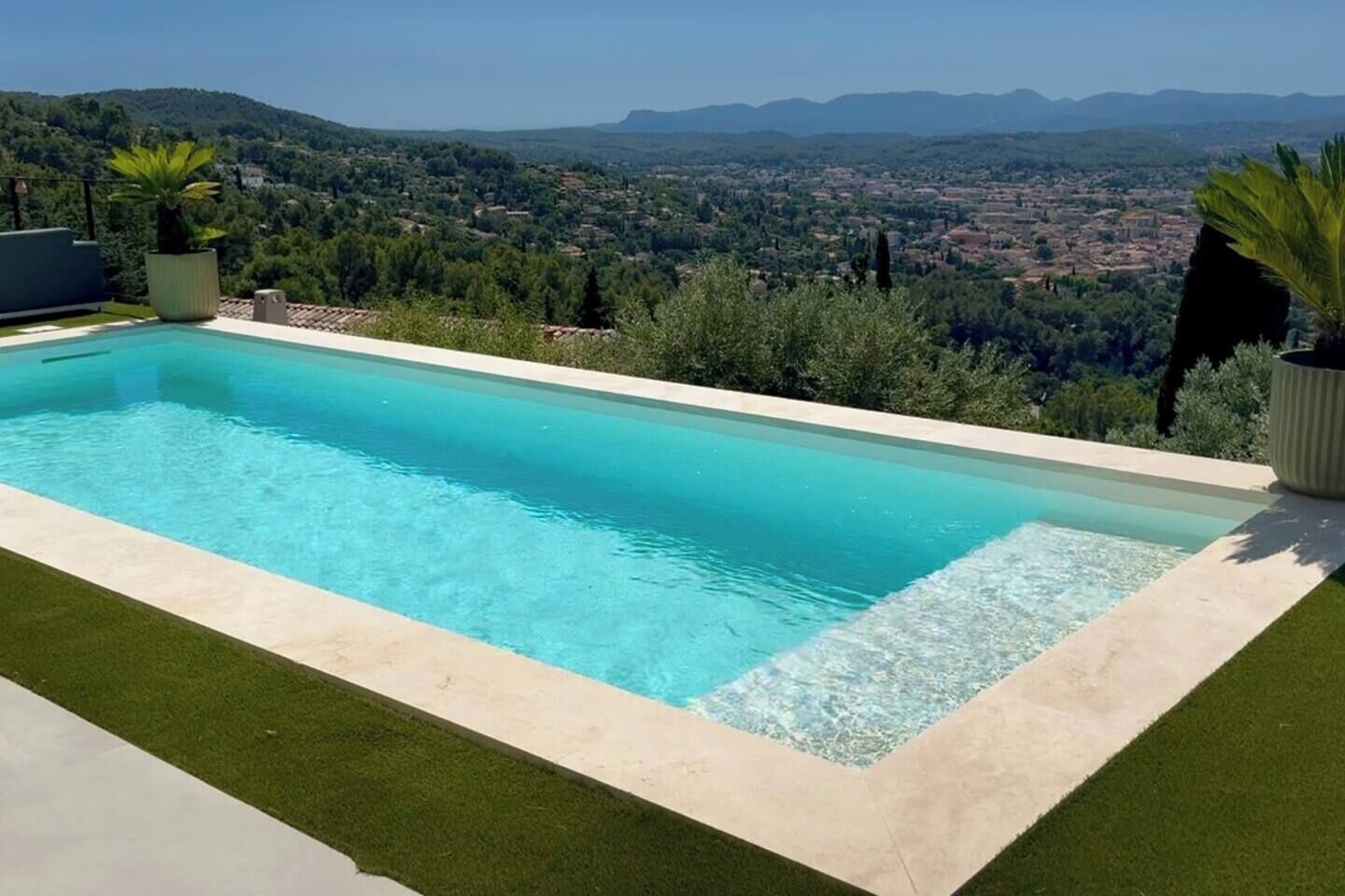 A rectangular swimming pool with clear blue water, surrounded by a light-colored deck and green artificial grass.