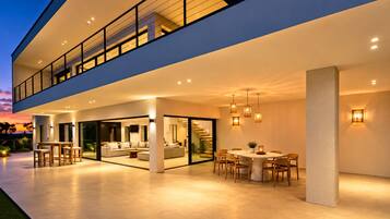 Une maison moderne à deux étages dotée d’un espace repas extérieur, d’un balcon et d’un escalier menant à l’étage supérieur.
