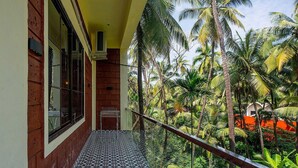 A balcony with a patterned floor, a glass railing, and a view of palm trees and a building in the background. - Palette Orient Greenz Pench by Checkin (Kurai)