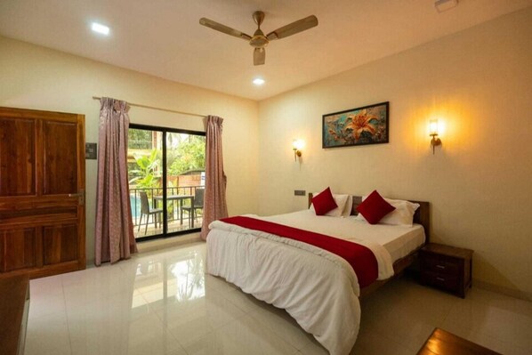 A hotel room with a large bed, a ceiling fan, a painting on the wall, and a view of the outdoors through a sliding door. - Palette Orient Greenz Pench by Checkin (Kurai)