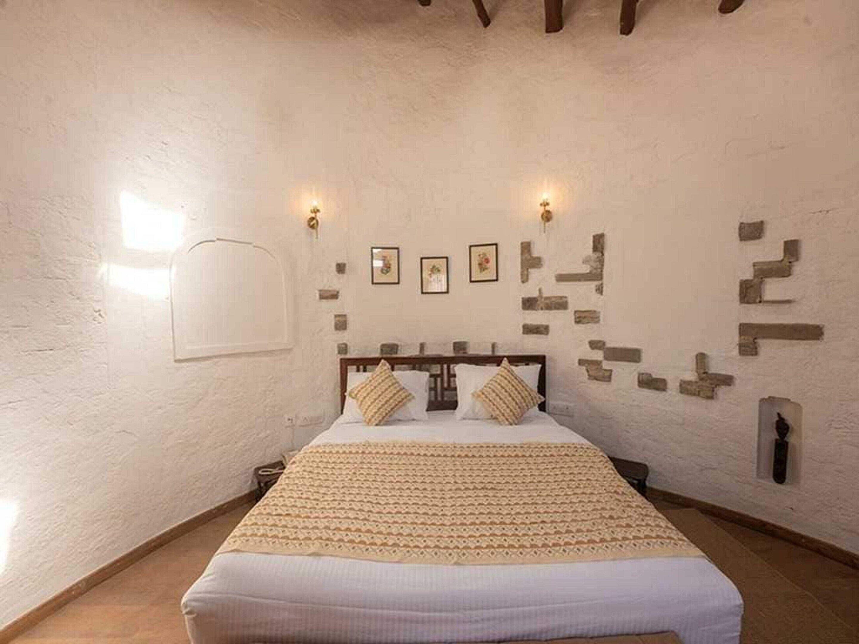 A bedroom with a bed, a wooden headboard, a patterned bedspread, and wall-mounted lights.