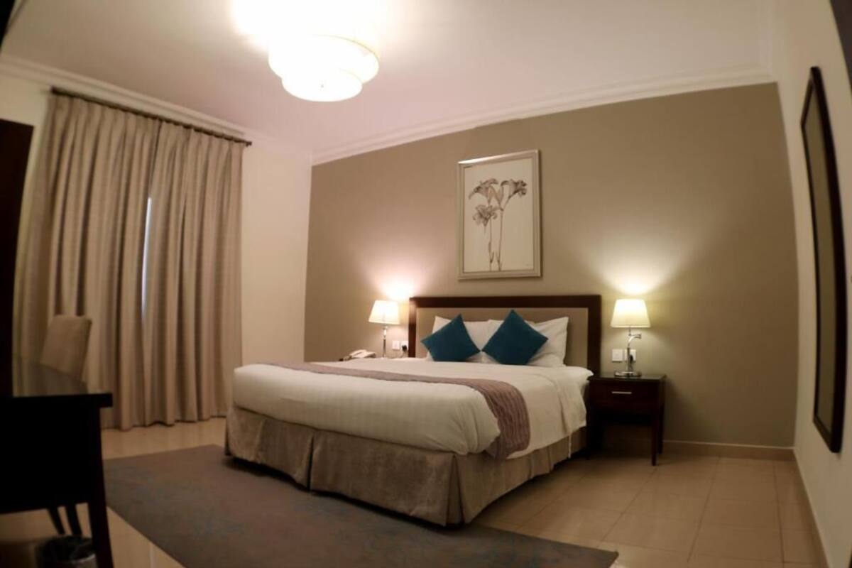 A hotel room with a large bed, two bedside lamps, a nightstand, a chair, and a window with curtains.