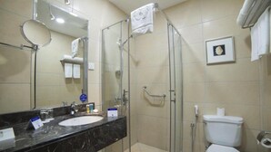 Une salle de bain avec une douche à parois de verre, des toilettes blanches, un lavabo avec un plan de toilette en marbre et un miroir.