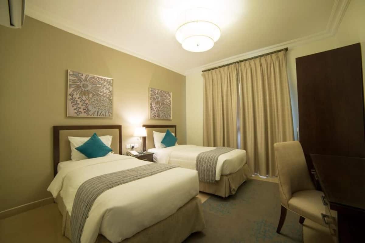A hotel room with two beds, a desk, a chair, and two wall art pieces.