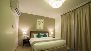 Une chambre d’hôtel avec un lit, deux lampes de chevet, une table de chevet, un appareil de climatisation, un tableau encadré au mur et une fenêtre avec des rideaux.