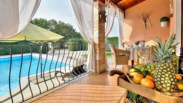 Een balkon met een zwembad, witte gordijnen en een tafel met fruit.