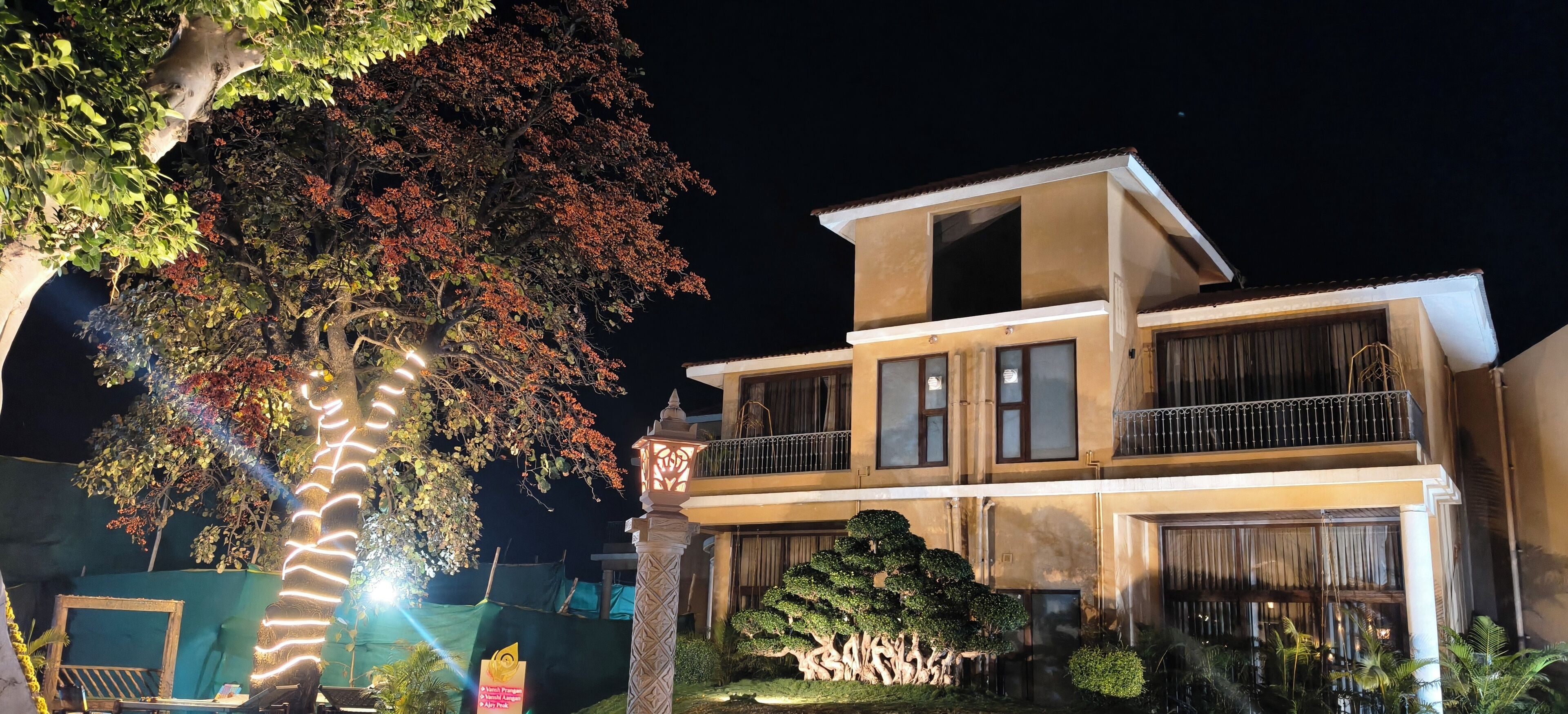A two-story building with a balcony on the upper level, surrounded by trees and well-lit at night.