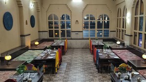 A restaurant with multiple tables set for dining, featuring traditional decor and large windows. - Vaikunth Village Resort (Abhanpur)
