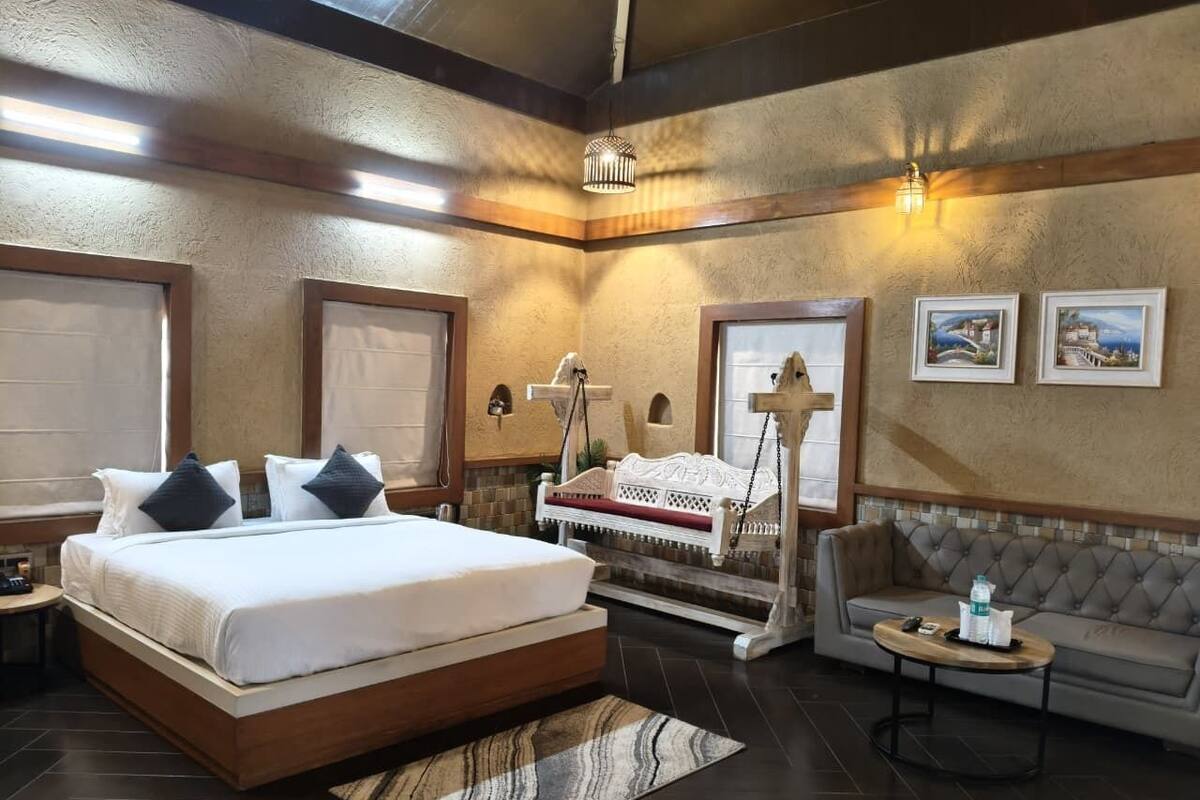 A modern hotel room with a large bed, a sofa, a small table, and a swing chair.
