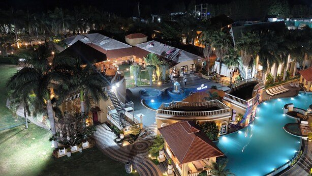 An aerial view of a resort with multiple swimming pools, palm trees, and well-lit pathways. - Vaikunth Village Resort (Abhanpur)