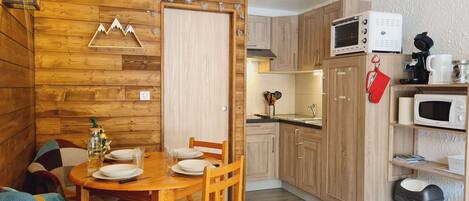 A wooden interior with a dining table set for four, a kitchen with wooden cabinets and appliances, and a decorative wall with a mountain and heart shapes.