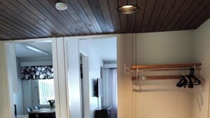 Una habitación con techo de madera, alfombra gris, una silla de madera y un perchero con ganchos.