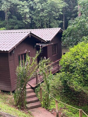 A wooden cabin with a sloped roof, surrounded by dense greenery and a staircase leading to the entrance. - Cabana da Lagoa (Santo Amaro da Imperatriz)