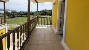 Un balcon abrité, doté d’un sol carrelé, d’une balustrade en bois et offrant une vue sur un paysage verdoyant.