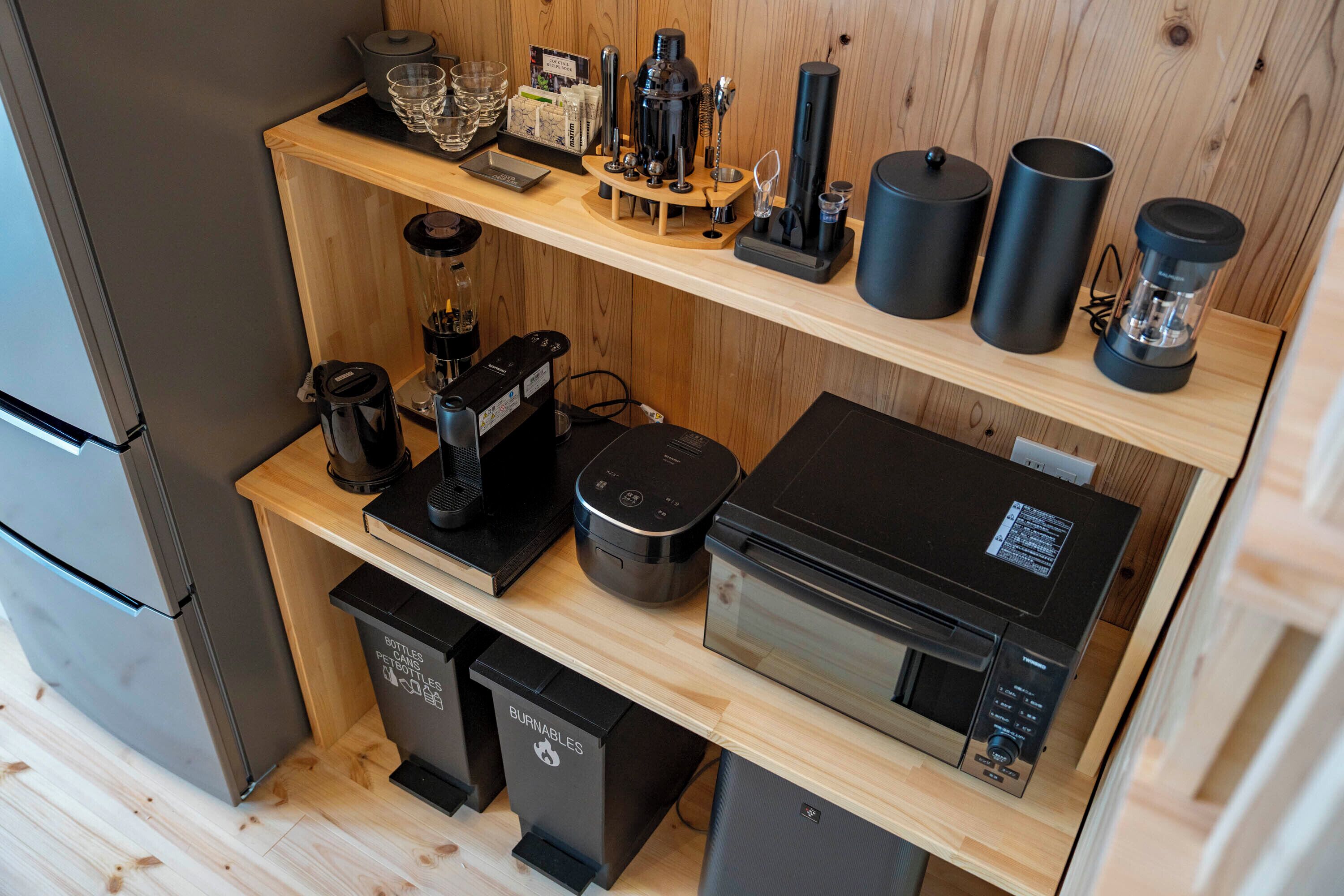 Une cuisine compacte équipée d’un réfrigérateur, d’une machine à café, d’un four à micro-ondes et d’une poubelle portant l’étiquette « DÉCHETS INCINÉRABLES ».