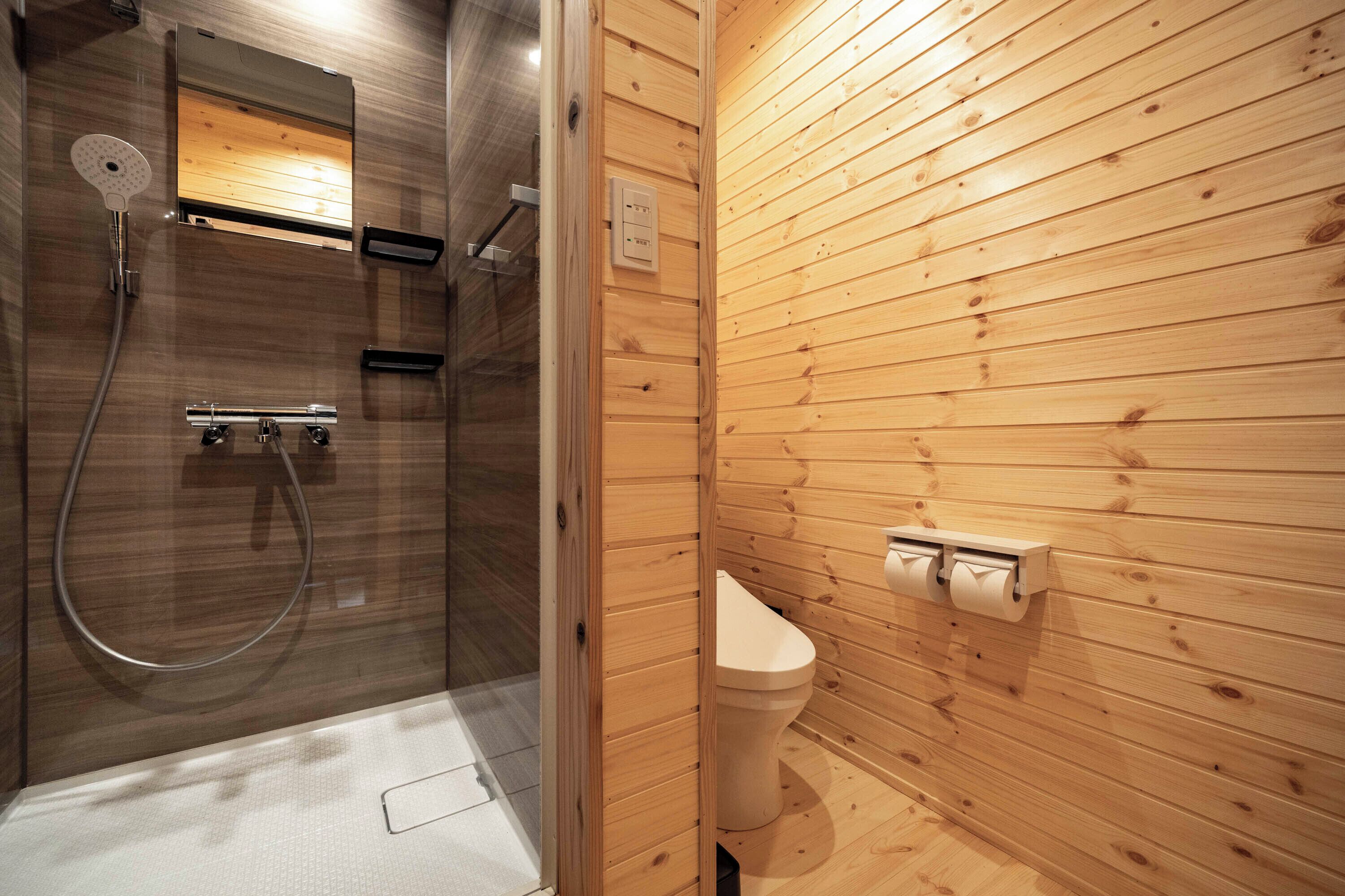 A wooden-paneled bathroom with a glass-enclosed shower, a toilet, and a wall-mounted towel dispenser.