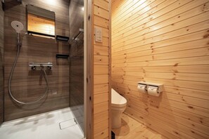 A wooden-paneled bathroom with a glass-enclosed shower, a toilet, and a wall-mounted towel dispenser.