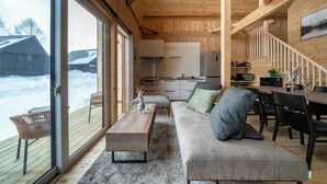 Een modern interieur met een houten plafond, een bank met kussens, een eettafel en een keukenhoek.