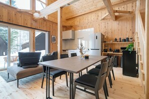 A modern wooden interior with a dining area, kitchen, and large windows.