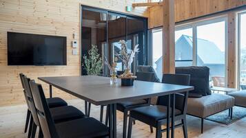 A modern dining area with a large table, black chairs, and a television mounted on the wall.
