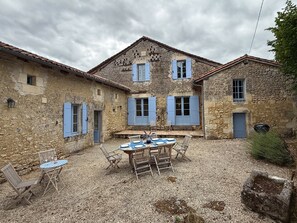 A stone building with blue shutters, a gravel courtyard, and outdoor seating. - Beautifully restored Farmhouse in the heart of the countryside with private pool (Bourg des Maison)