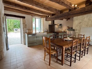 A rustic kitchen with wooden beams, a dining table with chairs, and a view of the outdoors.