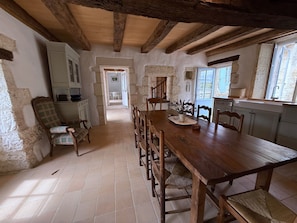 A rustic dining area with a wooden table and chairs, stone walls, and a view of the outside.