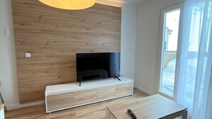 Ett modernt vardagsrum med en väggpanel i trä, en platt-TV, ett vitt konsolbord och ett litet bord med en fjärrkontroll.
