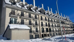 Un hotel de varios pisos con balcones, tejados cubiertos de nieve y un cielo azul despejado.