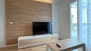 Un soggiorno moderno con una TV a schermo piatto montata su una parete in legno, un tavolino consolle bianco e un pavimento in legno.