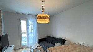 Un soggiorno moderno con un divano, un tavolo da pranzo, una TV e una finestra con vista sull'esterno.