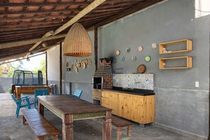 A rustic outdoor kitchen with a wooden table and benches, a hanging light fixture, and decorative plates on the wall. - Porto de Galinhas - Serrambi Beach with swimming pool 280m from the sea. (Camela)