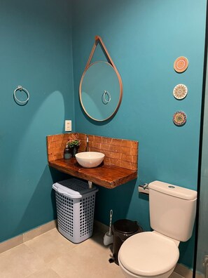 A bathroom with a teal wall, a wooden vanity, a white sink, a toilet, and a laundry basket. - Porto de Galinhas - Serrambi Beach with swimming pool 280m from the sea. (Camela)