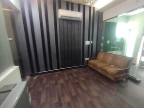 Une pièce avec un plancher en bois foncé, un canapé en cuir marron et un mur à rayures noires et blanches.