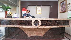 A reception desk with a marble design, a potted plant, and a calendar on the wall. - Townhouse GE Road Raipur Formerly Ratan (Raipur)