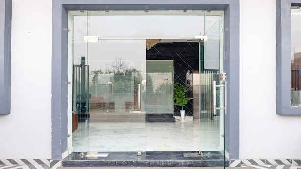 Une entrée moderne avec une porte en verre, un pot de fleurs et un portail en métal.
