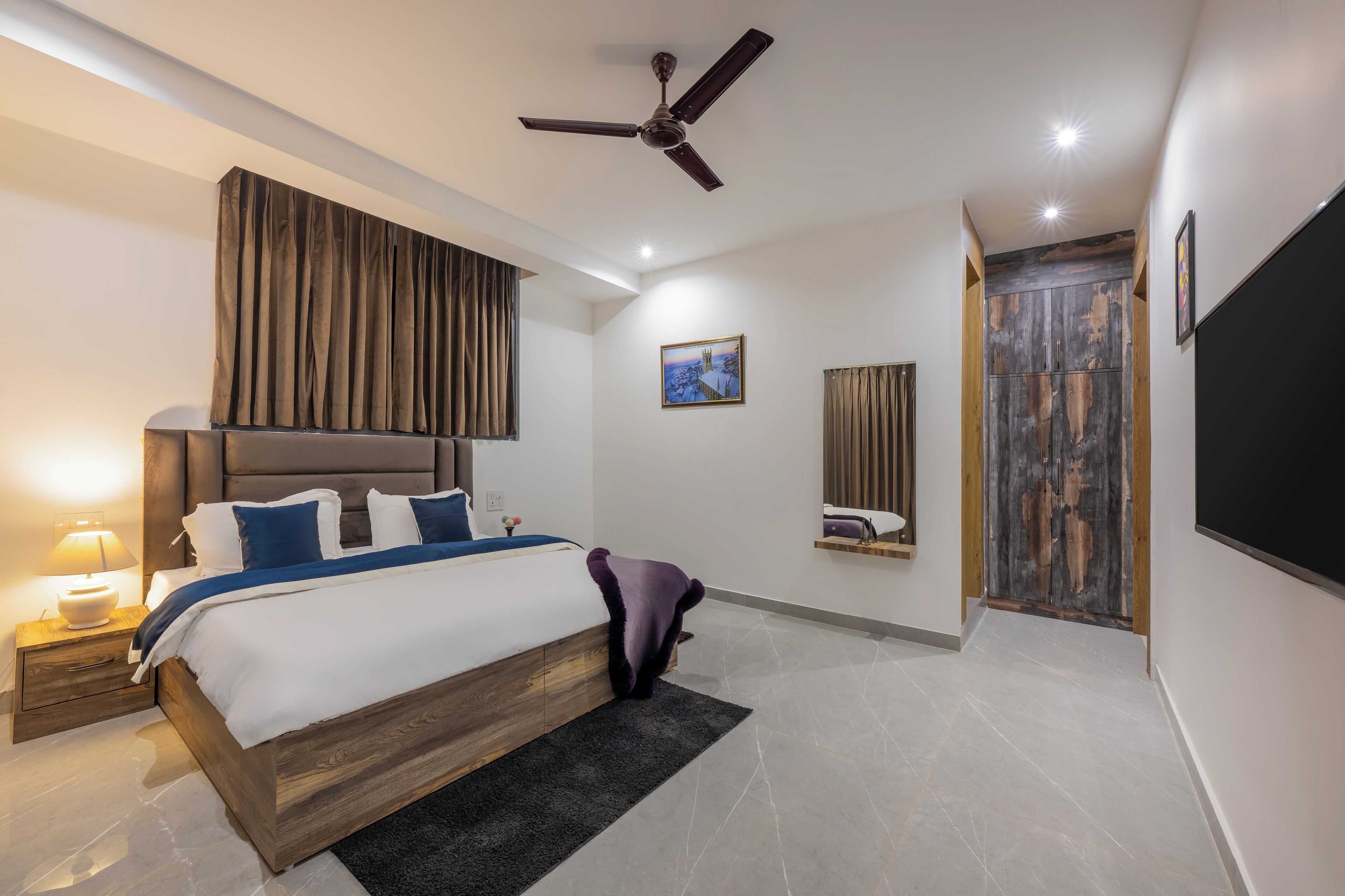 Un dormitorio moderno con una cama grande, un ventilador de techo, una mesita de noche con lámpara y un armario de madera.
