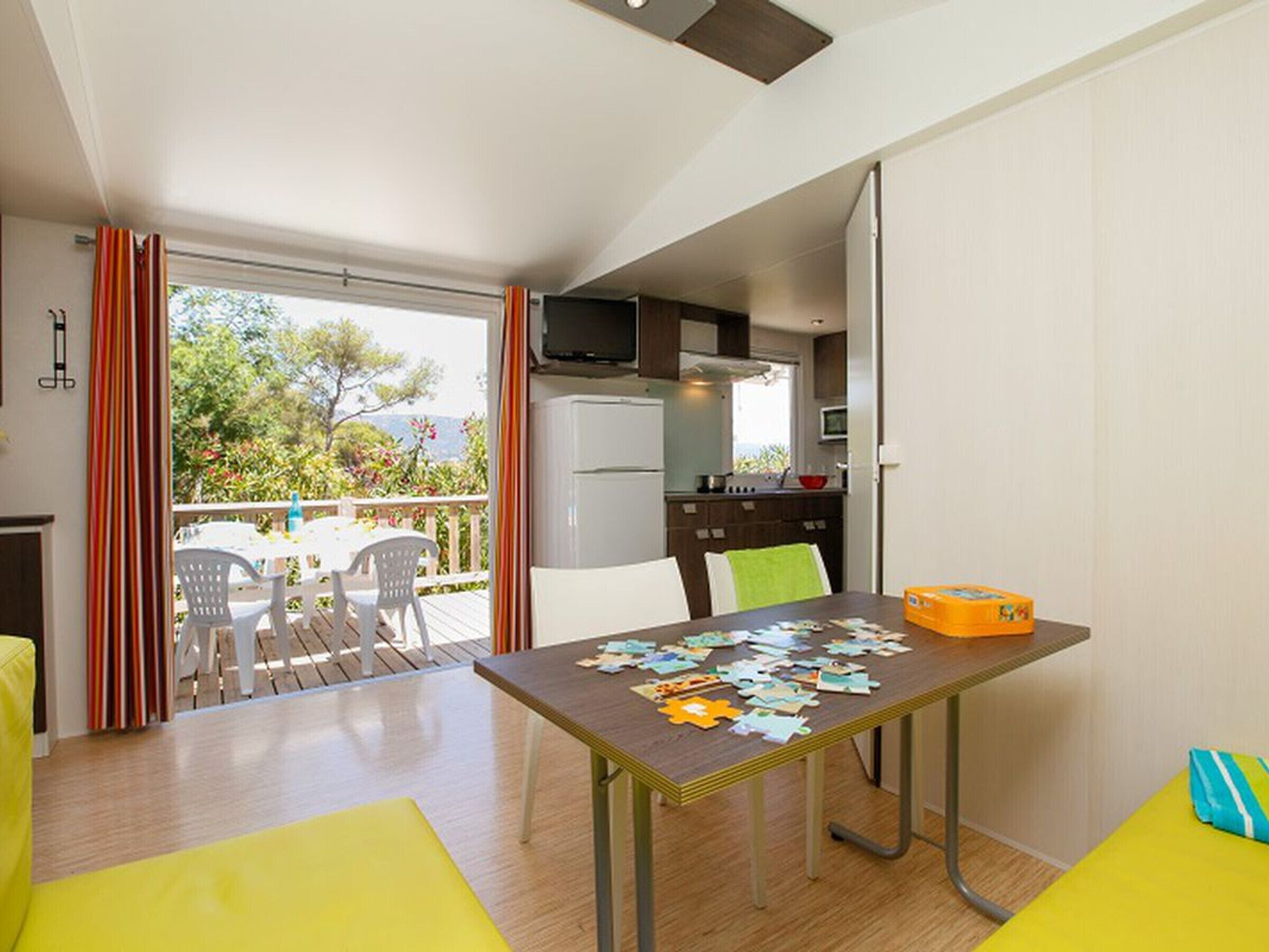 Quarto moderno com uma mesa de jantar coberta de papéis, área de cozinha com armários e eletrodomésticos, e varanda com cadeiras e uma mesa.