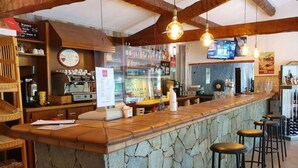Een bar met een stenen toonbank, krukken en een televisiescherm.