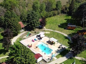An aerial view of a residential area with a swimming pool, a covered patio, and a small building with a red roof.