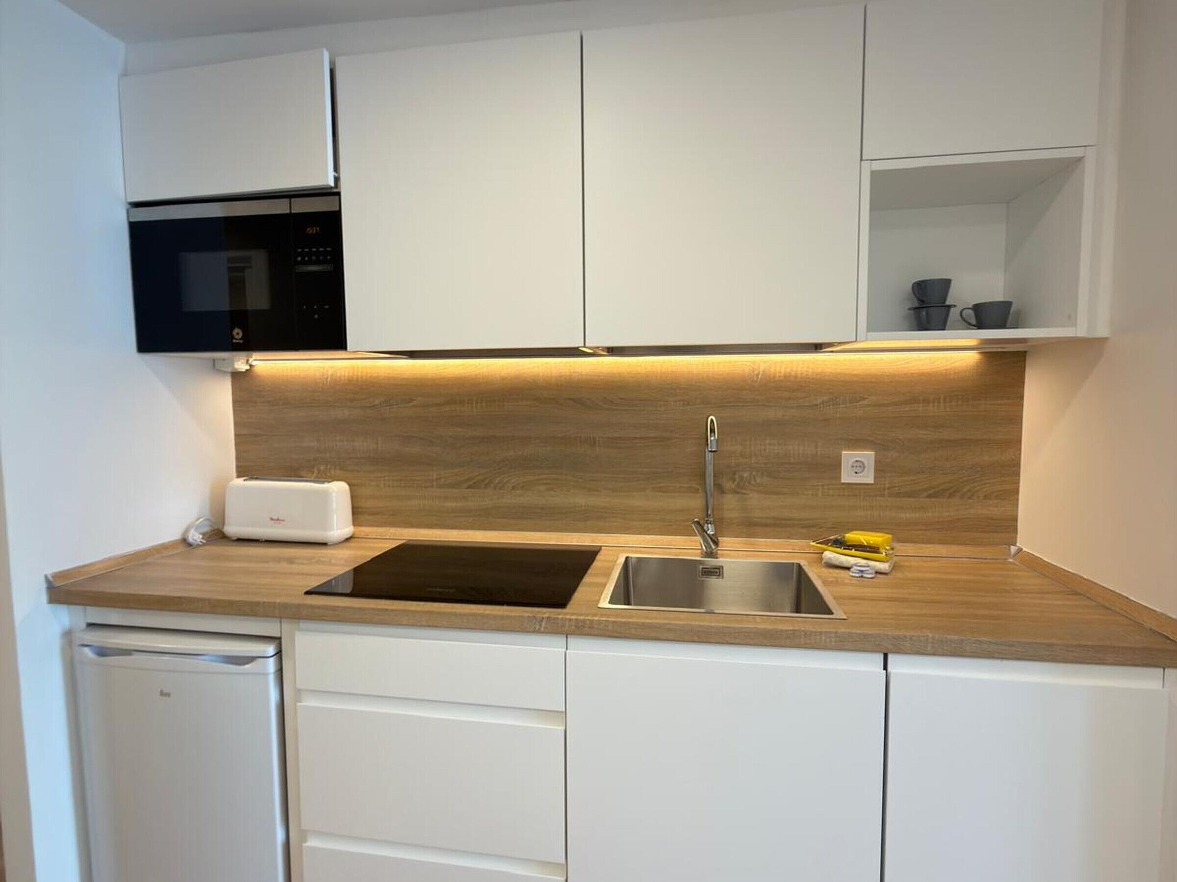 Een moderne keuken met witte kasten, een houten aanrechtblad, een ingebouwde magnetron en een roestvrijstalen spoelbak.