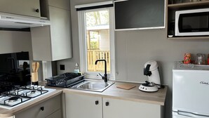 A compact kitchen with a gas stove, a sink, a microwave, and a refrigerator. - Mobile Home with Terrace, Ideal for 4 (Arvert)