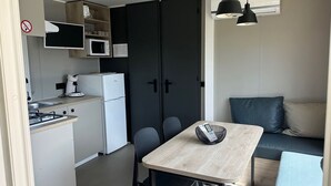 A compact kitchenette with a microwave, stove, and refrigerator. There is a dining table with chairs and a sofa with a cushion. - Mobile Home with Terrace, Ideal for 4 (Arvert)