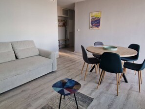 A modern living room with a sofa, a round dining table with chairs, a small side table, and a poster on the wall. - Quiet T2 Apartment, 4 Pers, Parking (Banyuls-sur-Mer)