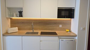 Une cuisine compacte avec des meubles blancs, un four à micro-ondes encastré, un grille-pain et un lave-vaisselle.