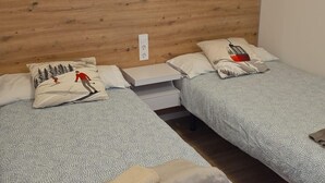 Une chambre avec deux lits, chacun agrémenté d’une couvre-lit et de coussins à motifs, d’une tête de lit en bois et d’une table de chevet blanche.