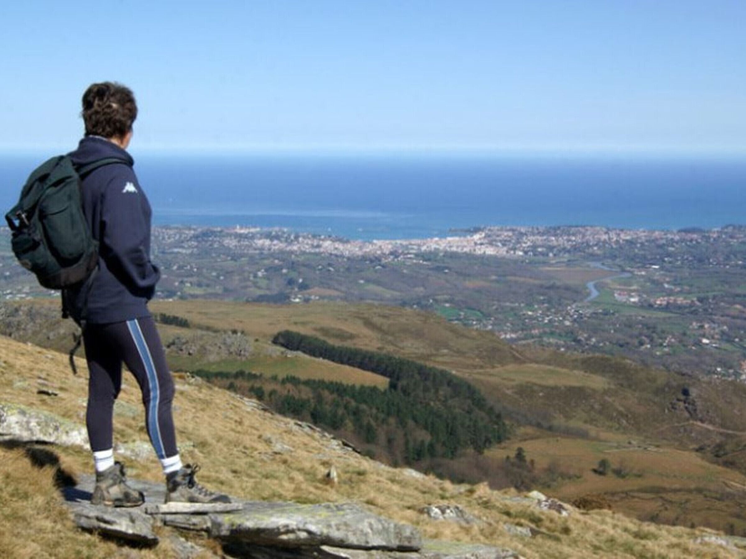 Una persona de pie sobre un promontorio rocoso con vistas a un pueblo costero.