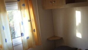 Une chambre à coucher avec un lit, des oreillers, une fenêtre avec des rideaux et une petite étagère.